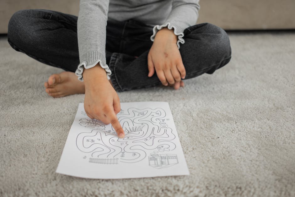 Crop anonymous barefooted child sitting on floor with crossed legs and solving labyrinth puzzle at home